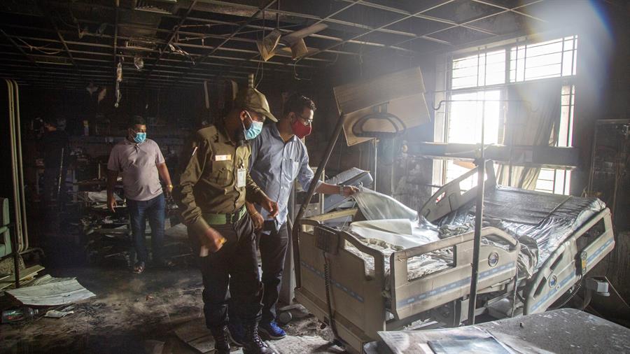 Hospital em Bangladesh destruído por incêndio com três homens olhando para uma cama
