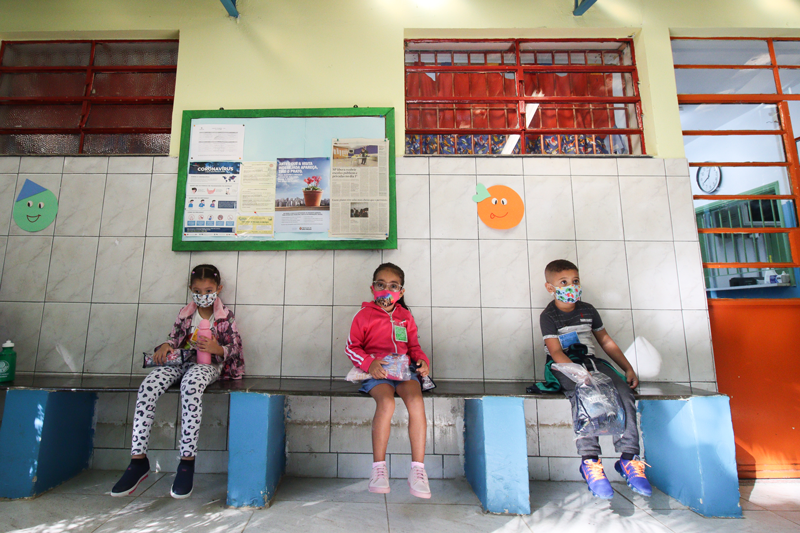 Crianças sentadas em um banco no pátio da escola, na cidade de São Paulo