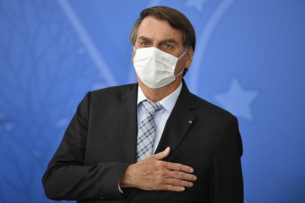 De terno, gravata e máscara de proteção, Bolsonaro leva a mão ao peito