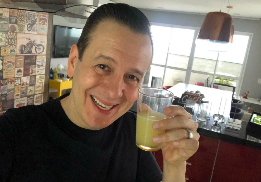 Selfie de Celso Zucatelli em sua casa com um copo de suco na mão