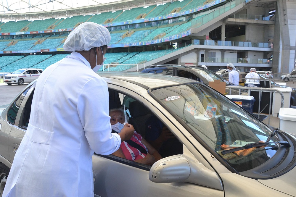 Enfermeira aplica vacina em uma idosa que está dentro de um carro parado no estádio da Fonte Nova