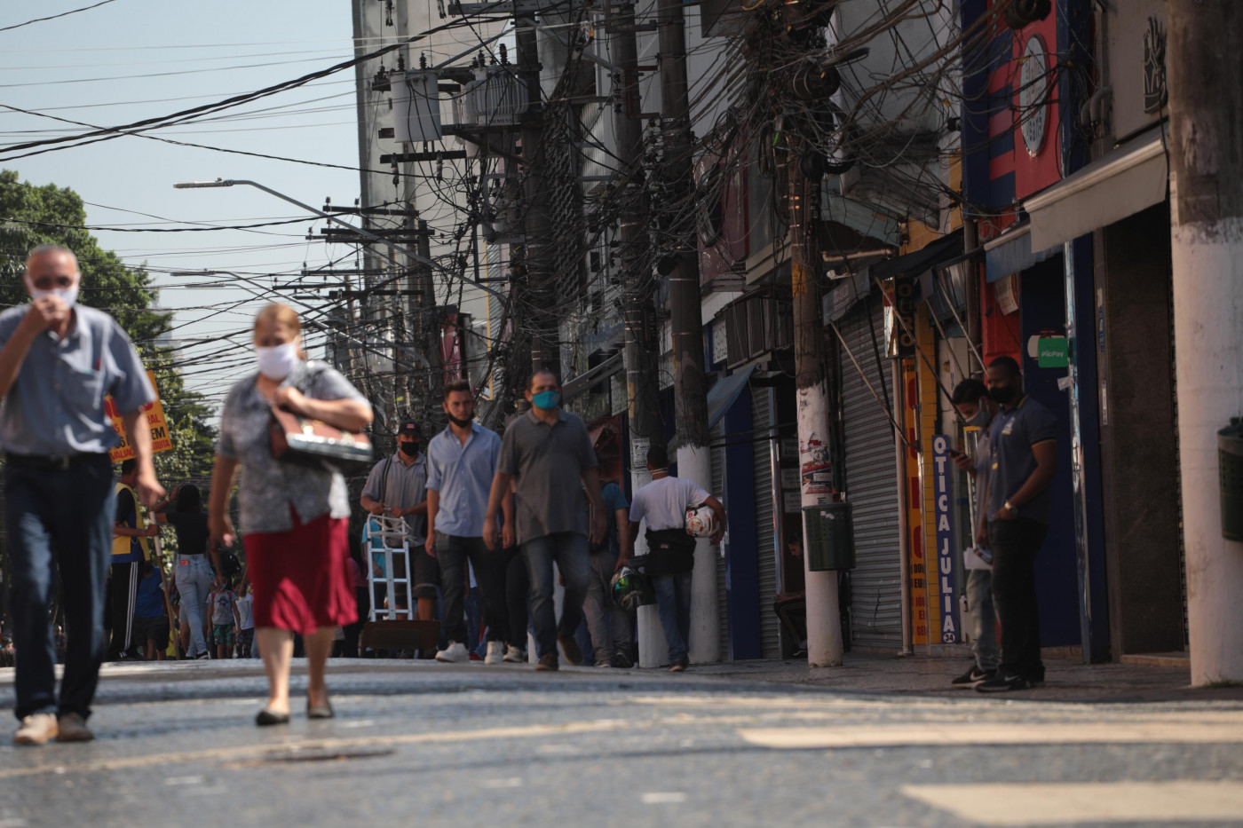 Pessoas andando na rua de máscara no bairro Santo Amaro, em São Paulo, enquanto as lojas estão fechadas