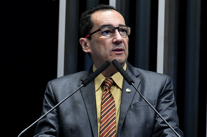 Senador Jorge Kajuru. Homem branco de óculos, terno azul e camisa amarela. Gravata listrada vermelha e azul escuro