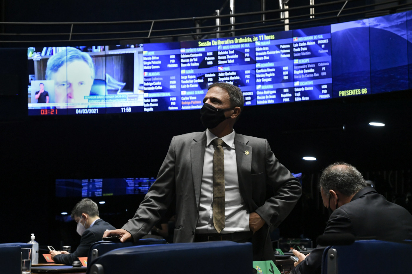 De terno e gravata, o senador Márcio Bittar aparece em primeiro plano com o placar do Senado ao fundo