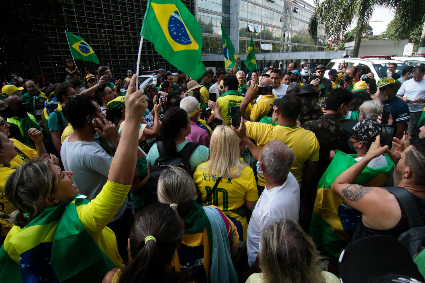 Pessoas usando camisa do Brasil e hasteando bandeira do Brasil durante aglomeração na rua