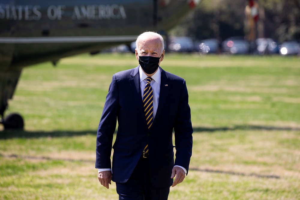 O presidente Joe Biden caminha em um gramado em Washington após descer do helicóptero, visto parcialmente ao fundo na imagem