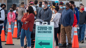 Pessoas esperando na fila para serem vacinadas nos Estados Unidos. Uma placa escrita 'Vacinação contra Covid-19' mostra a direção da fila
