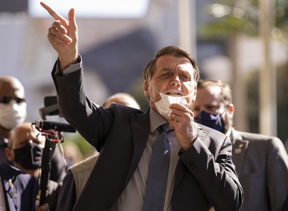 Com a máscara no queixo e a mão direita apontada para cima, em sinal de arma, Jair Bolsonaro caminha em Chapecó