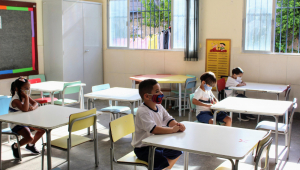 Quatro crianças sentadas na carteira escolar, uma distante da outra, assistem a uma aula em escola do Rio de Janeiro