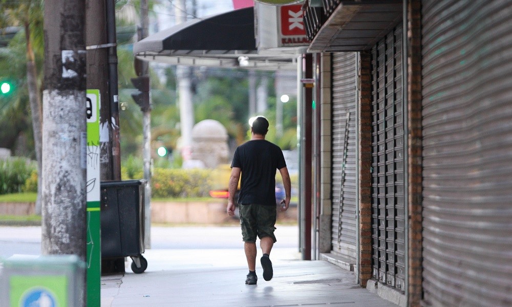 Com comércios fechados ao redor, Homem anda em calçada de Santos
