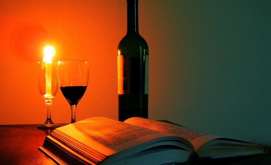 garrafa de vinho, taça com meio copo cheio e livro. vela acesa