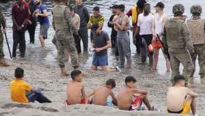 Soldados formam um cordão de isolamento em praia de Ceuta enquanto jovens marroquinos aguardam de pé ainda dentro d'água