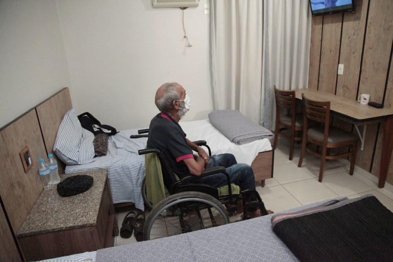 Imagem de um idoso em uma cadeira de rodas dentro de o quarto de hotel