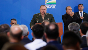 Posicionado atrás de um palco, o general Eduardo Pazuello fala para um público visto de costas na imagem (aparecem as cabeças dos presentes)