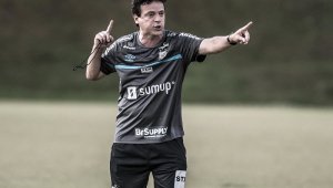 Com uma camisa cinza e um shorts preto do Santos, Fernando Diniz gesticula em um dos campos do CT Rei Pelé