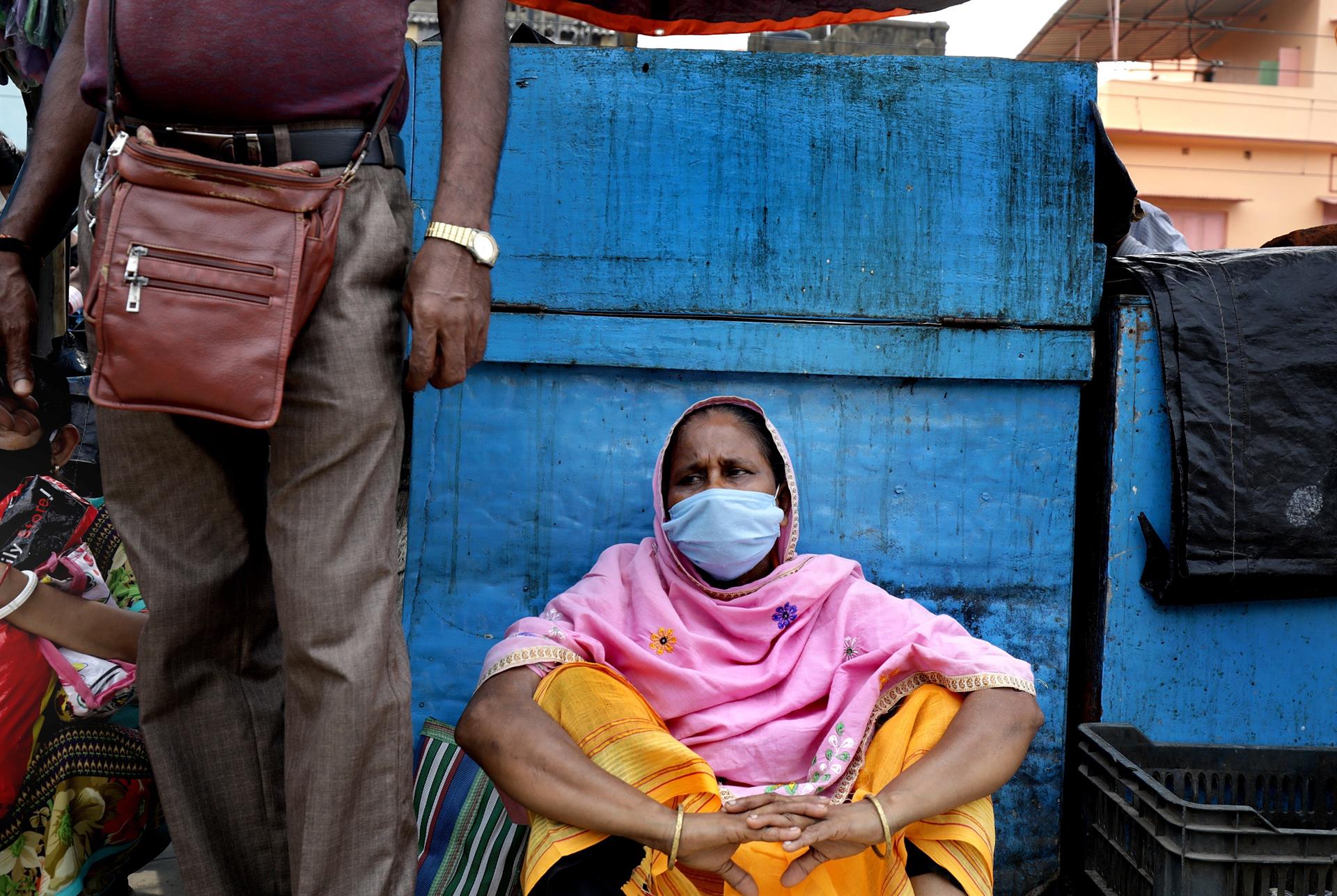 Usando máscara, mulher indiana senta-se no chão de estação de trem em Kolkata