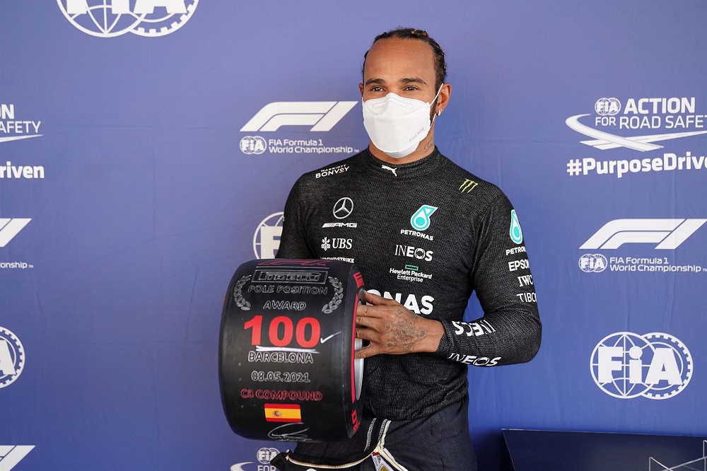 De máscara branca e macacão preto da Mercedes, Lewis Hamilton segura um troféu comemorativo em forma de pneu pelas 100 poles