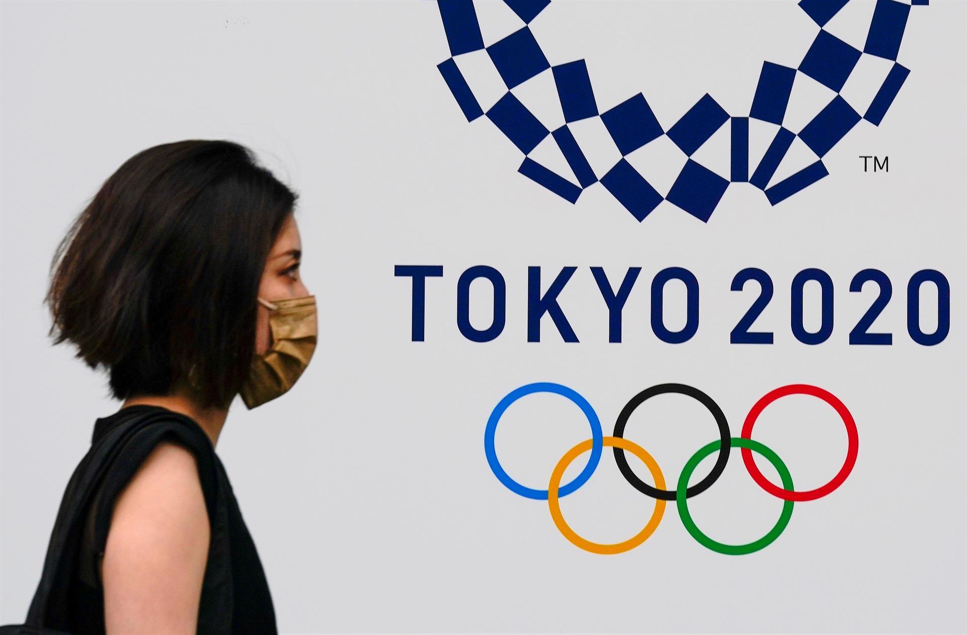 Mulher usando máscara de proteção facial passa diante de logo dos Jogos Olímpicos de Tóquio