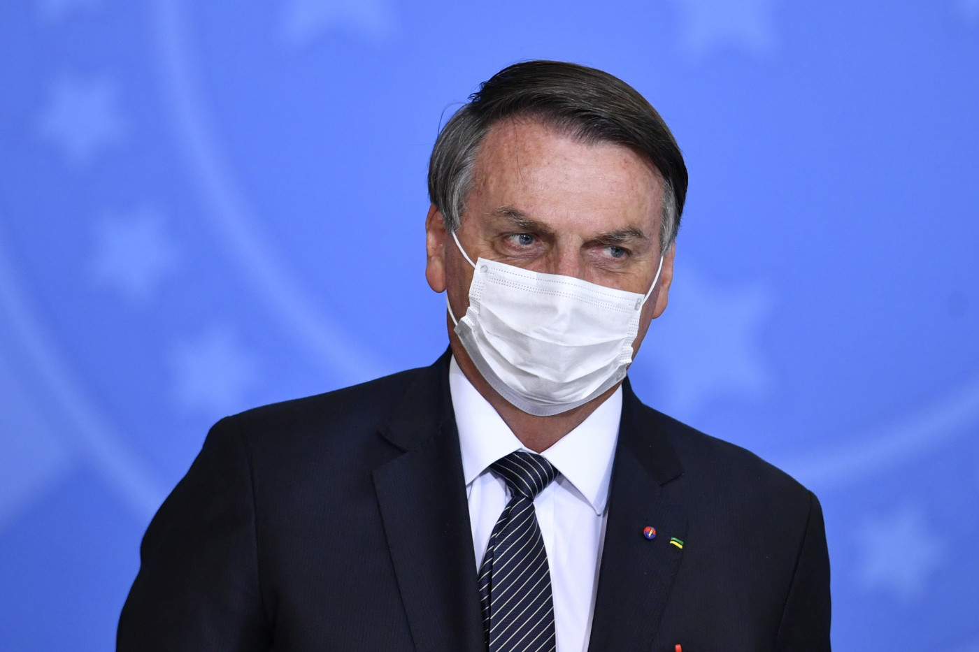 O presidente da República, Jair Bolsonaro, usa máscara de proteção branca e veste terno preto durante evento oficial