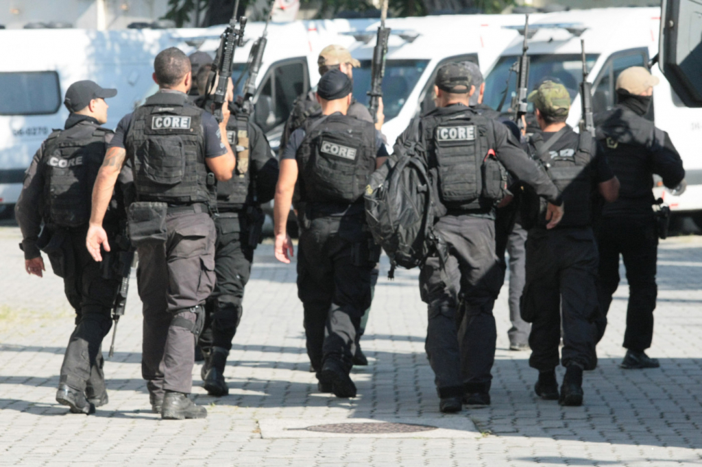 Vários policiais andando uns ao lado dos outros usando fardas e coletes pretos e empunhando armas