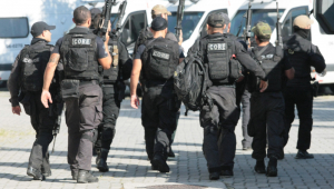 Vários policiais andando uns ao lado dos outros usando fardas e coletes pretos e empunhando armas