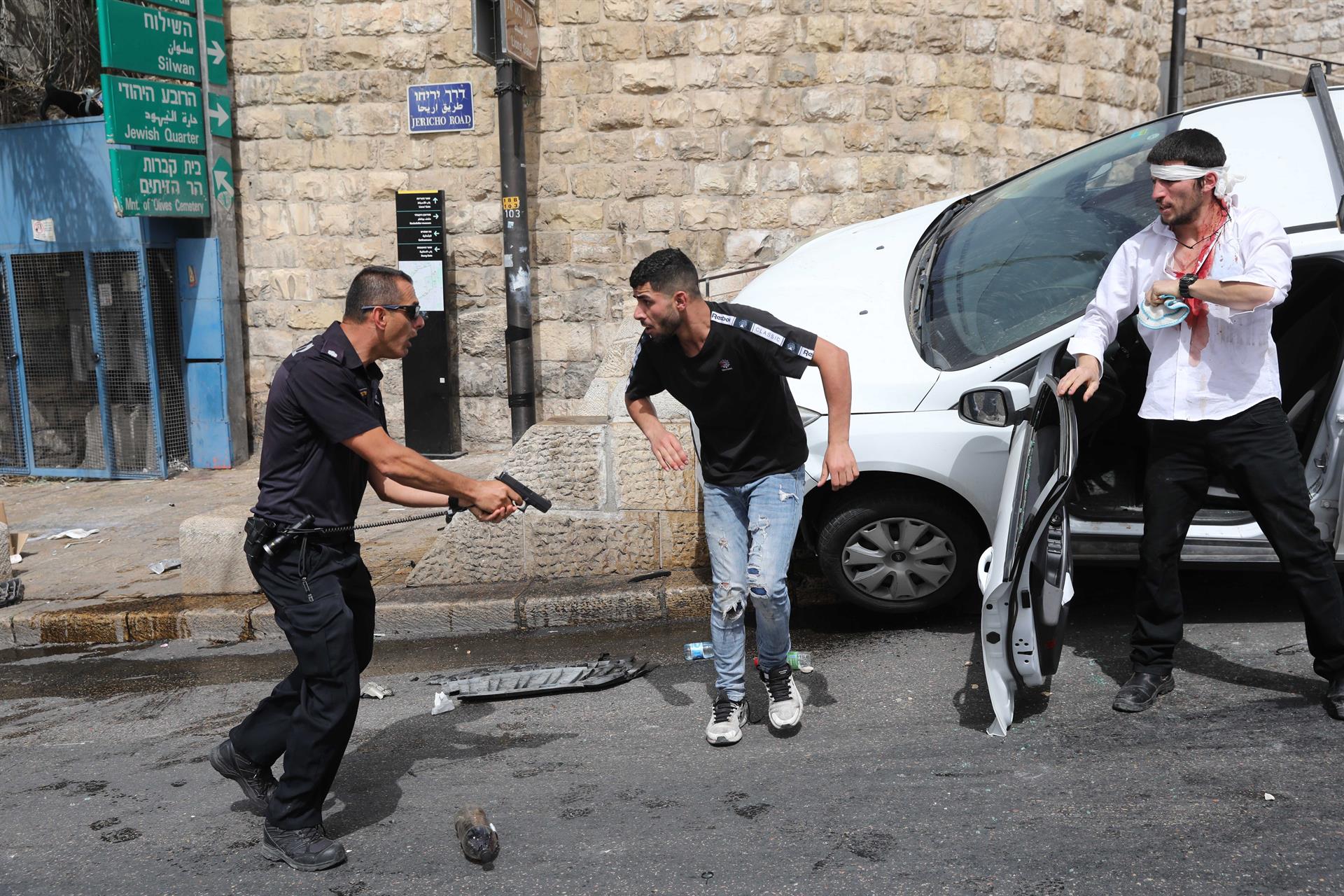 Policial israelense (esquerda) aponta arma para palestino (centro) ao lado de um judeu ortodoxo ferido (direita) em Jerusalém