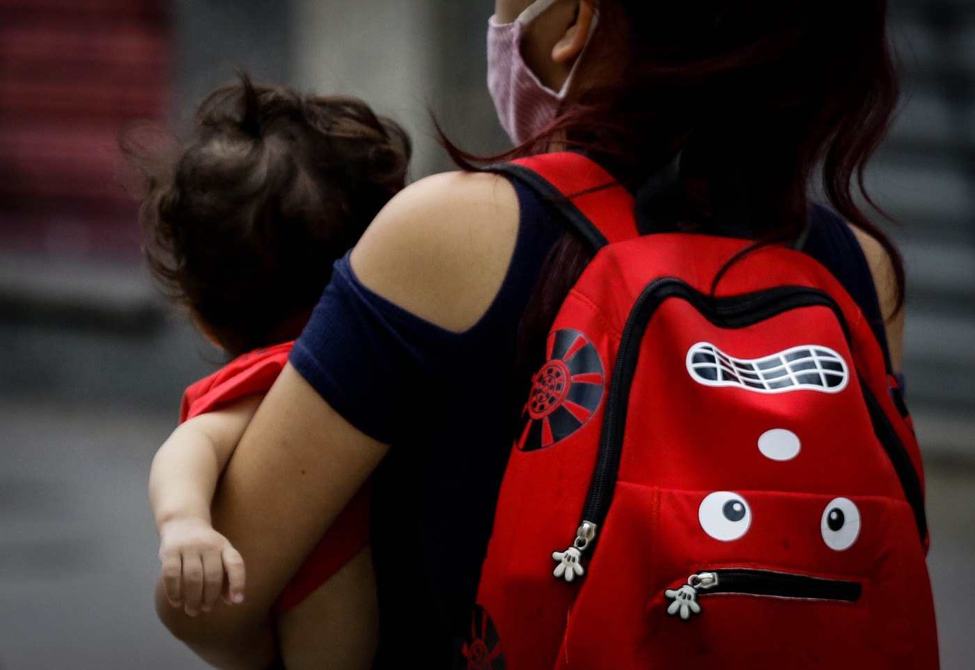 Imagem de uma mulher com uma mochila vermelha infantil segurando uma criança
