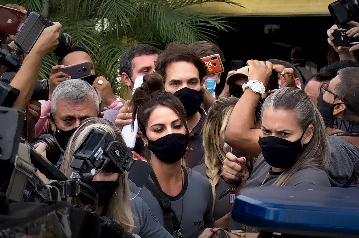 Monique Medeiros, mãe de henry borel, com multidão em volta. Ela usa blusa cinza, máscara de proteção preta e tem o cabelo preso em um rabo.