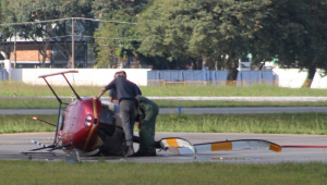 Dois homens vistoriam um helicóptero vermelho que caiu na pista do Campo de Marte