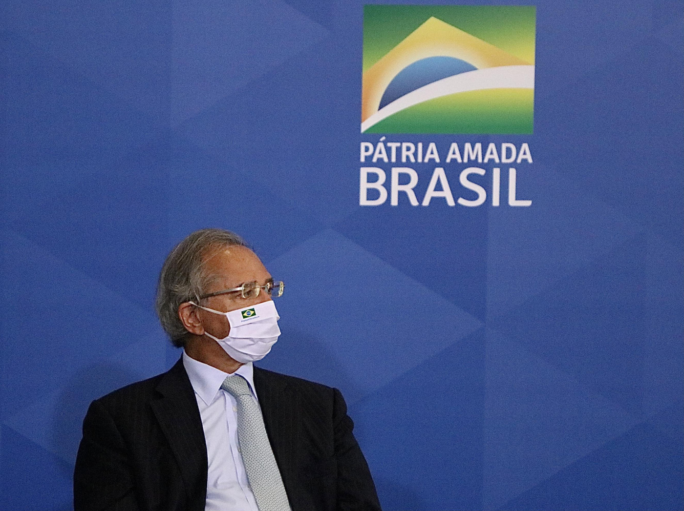 Paulo Guedes em frente um painel azul