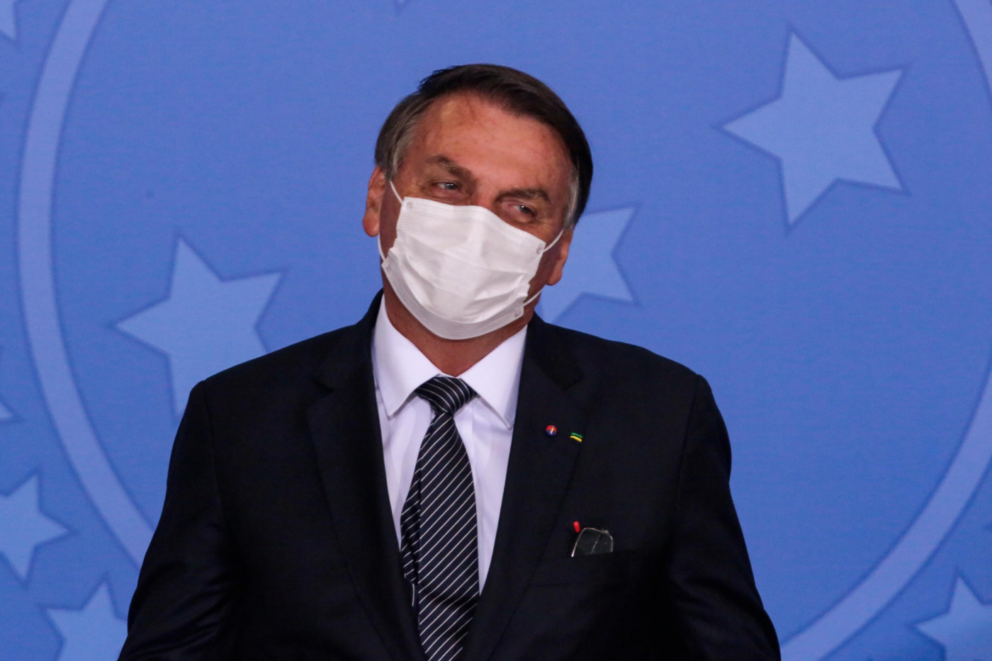 O presidente da República, Jair Bolsonaro, usa máscara de proteção branca e veste terno preto durante evento oficial