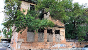 Sobrado antigo construído em uma esquina de São Paulo e aparentemente abandonado, com pichações na fachada e árvores que cortam as janelas