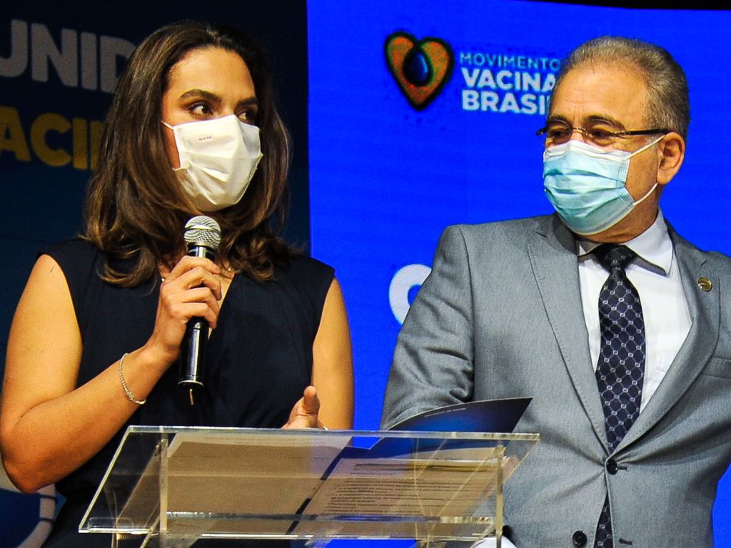 A médica infectologista Luana Araújo ao lado do ministro da Saúde, Marcelo Queiroga, ambos usam máscaras e Luana segura um microfone
