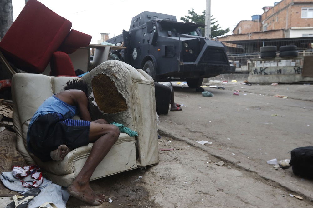 Em favela do Rio, morador se esconde atrás de sofá velho na calçada enquanto caveirão da polícia passa pela rua