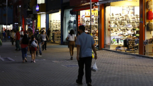 Com lojas abertas, a maioria de calçados, pessoas circulam à noite em calçada do centro de São Paulo