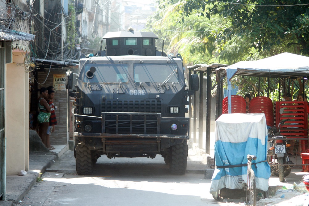 Carro blindado da polícia passa por rua estreita na favela do Jacarezinho e é observado por alguns poucos moradores