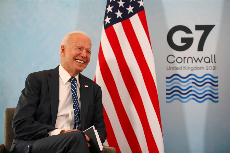 Presidente Joe Biden rindo. Ao fundo, a bandeira dos Estados Unidos e símbolo do G7