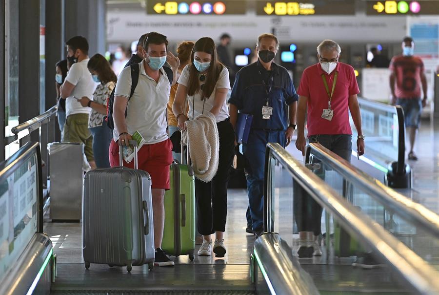 Turistas com máscaras e malas subindo na escada rolante de aeroporto Adolfo Suárez, na Espanha