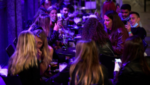 Dezenas de jovens namoram e conversam em um bar com mesas na calçada