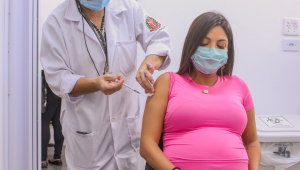 Mulher grávida de camisa rosa sendo vacinada