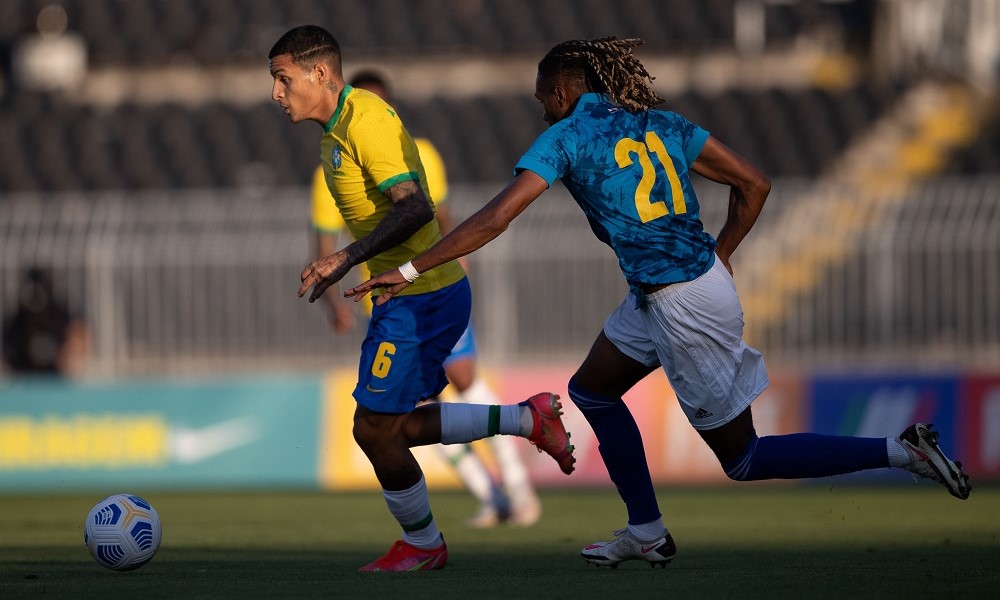 Marcado por Vasco Lopes, camisa 21 de Cabo Verde, que aparece de costas, Guilherme Arana parte com a bola dominada durante jogo da seleção olímpica