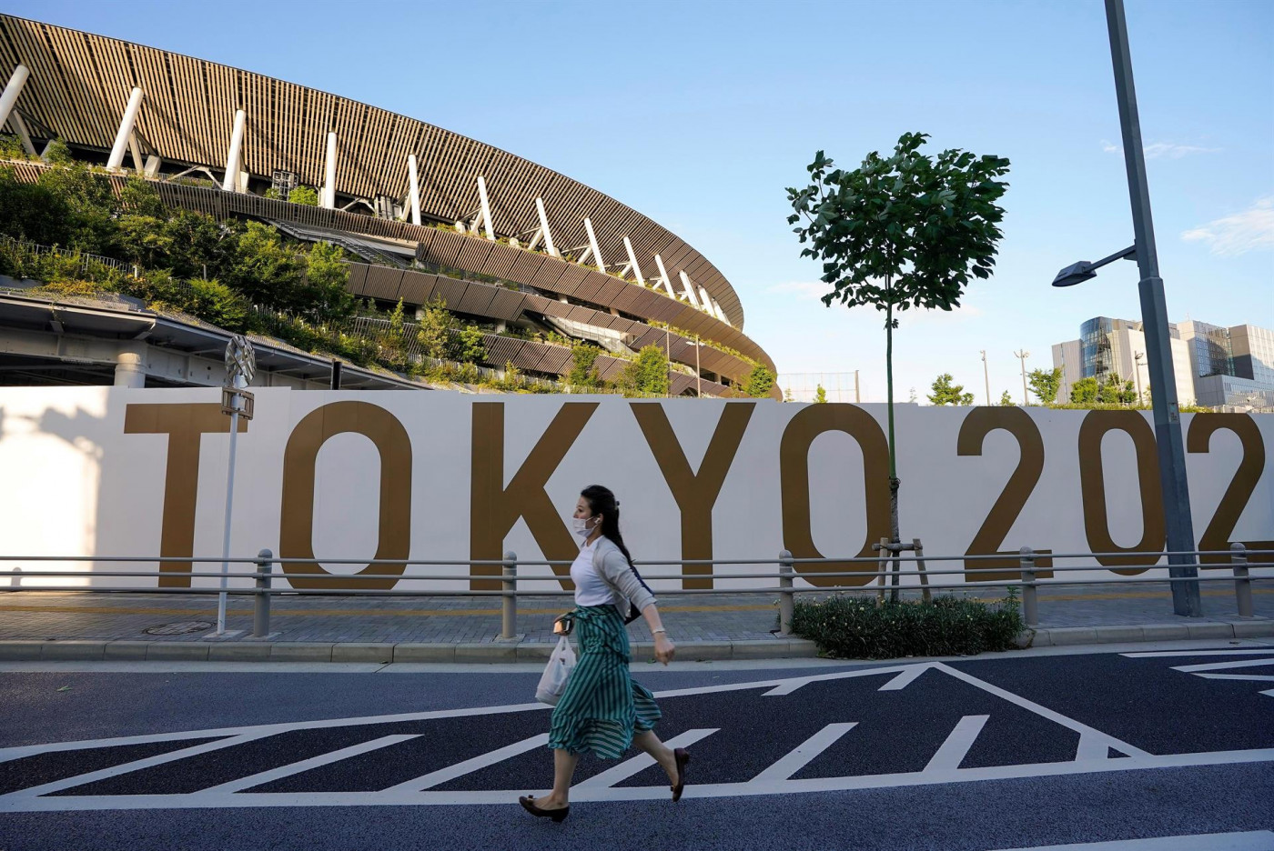 Mulher caminha em frente a banner escrito das Olimpíadas