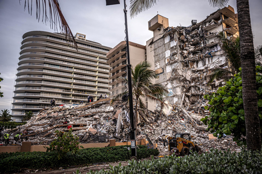 Vários destroços e uma parte desmoronada de um edifício grande em Miami. Ao lado, construções grandes ainda de pé.