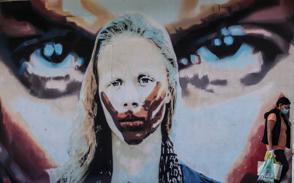 Mulher caminha diante de um grafite representando uma mulher sendo calada na Avenida dos Bandeirantes