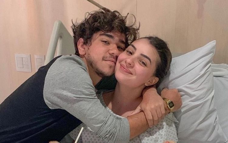 Mabel em uma cama de hospital e João Fernandes abraçado com ela