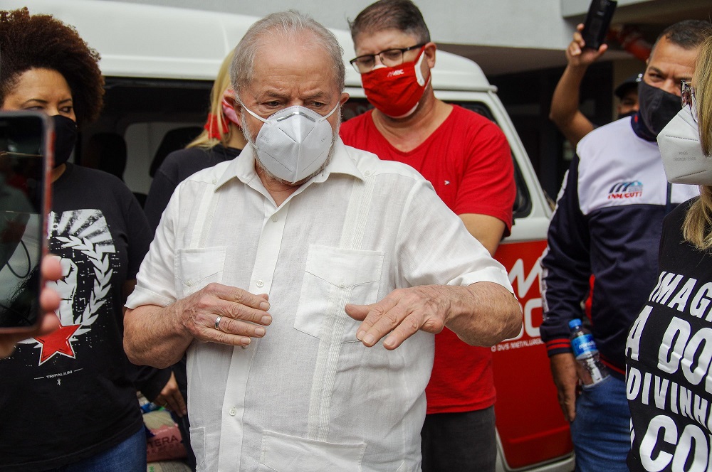 De máscara e camisa bege, Lula discursa rodeado por militantes do PT