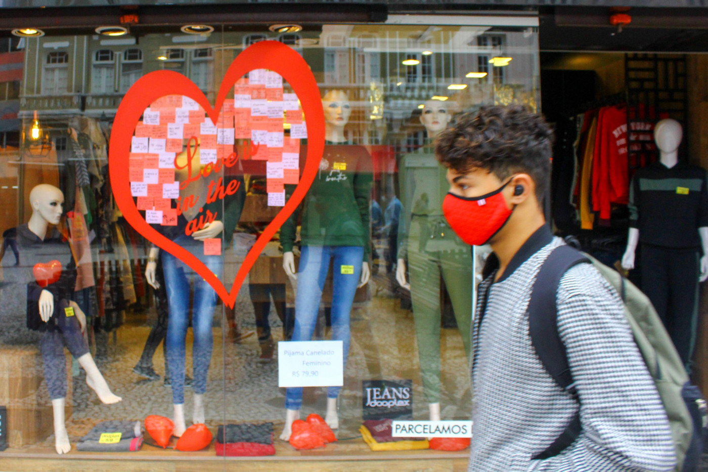 Usando máscara, homem passa na frente de uma loja com decoração para o dia dos Namorados