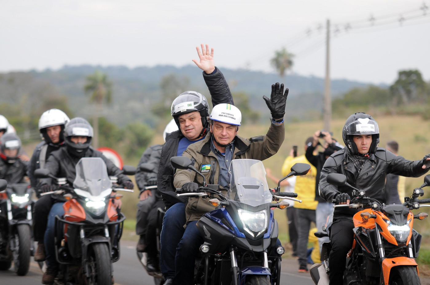 Presidente Jair Bolsonaro em cima de moto com o prefeito de Chapecó. Eles usam capacetes e fazem um sinal de 