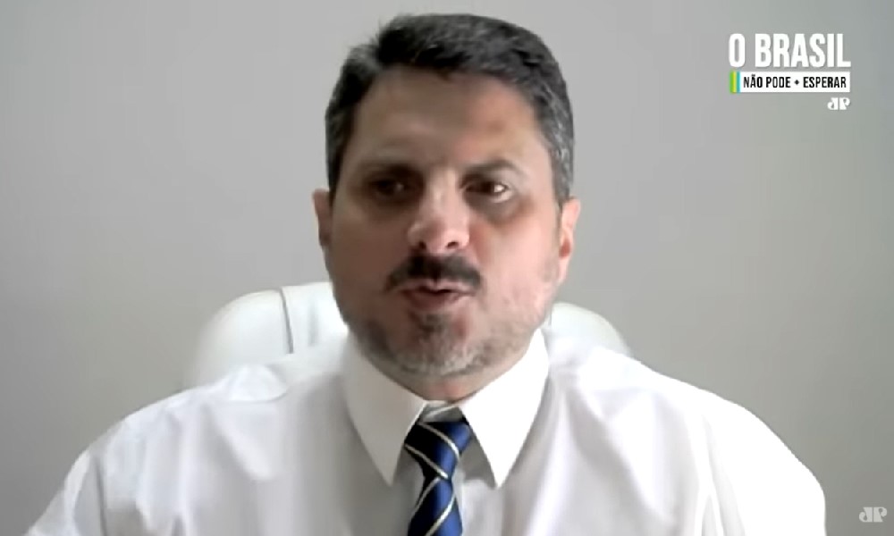 De camisa branca e gravata azul marinho estampada, o senador Marcos do Val, usando bigode e cabelo preto curto, grava depoimento à Jovem Pan