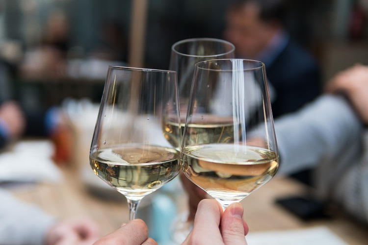 Mãos de três pessoas brindando com três taças pouco cheias de vinho branco